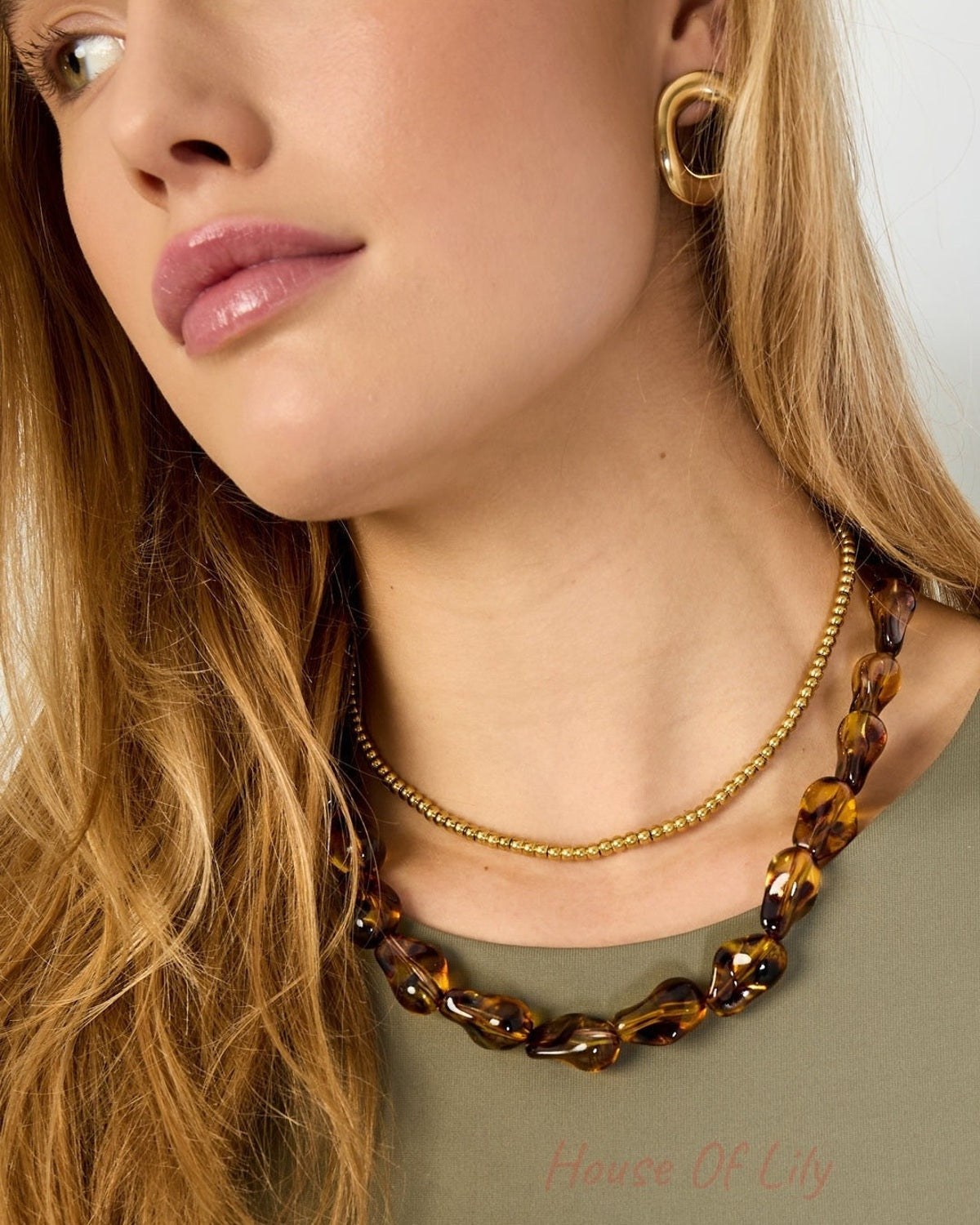Close-up side profile of woman wearing tortoiseshell acrylic necklace with gold earrings and olive green top