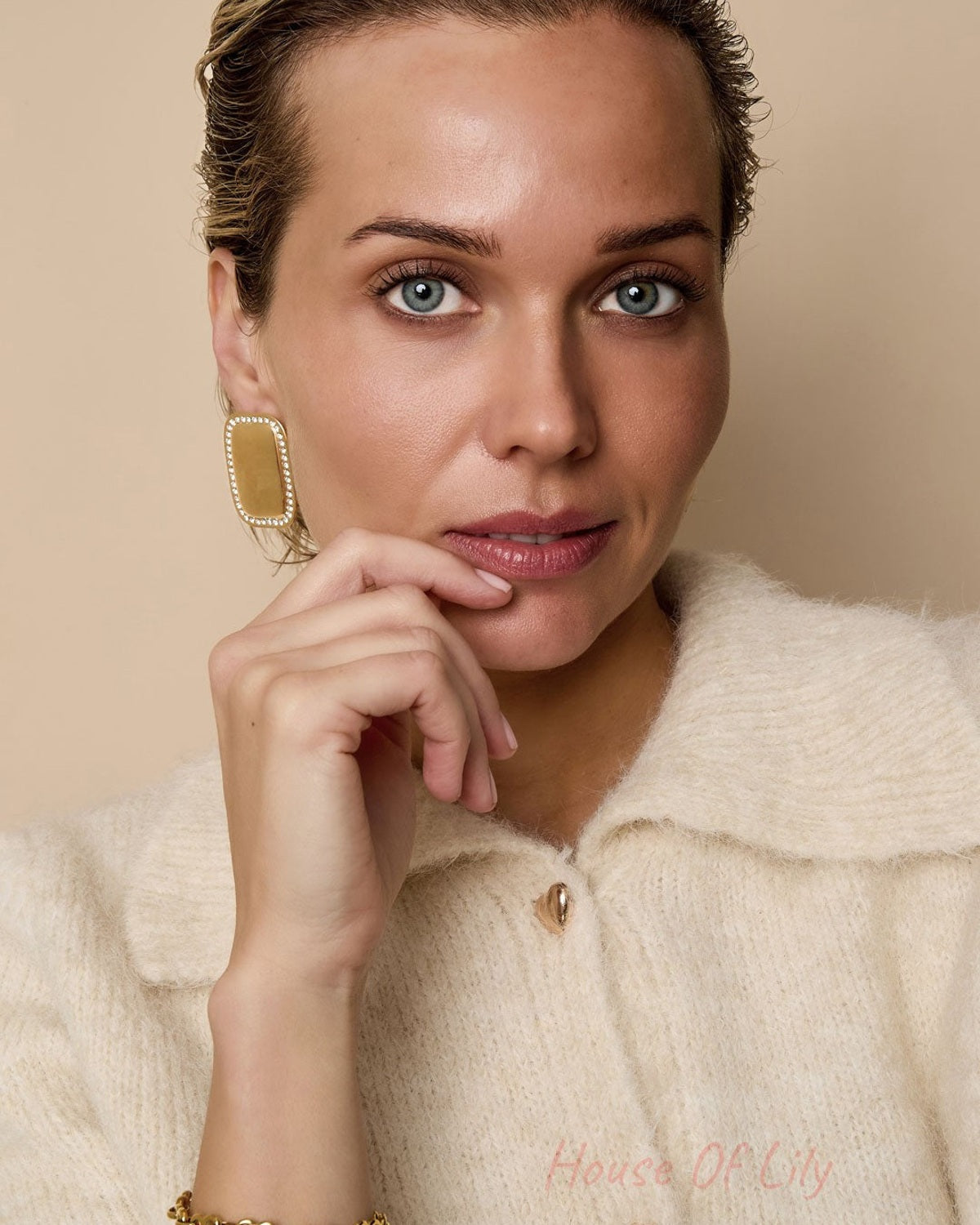 Close-up portrait of woman wearing the gold heart link bracelet and gold earrings, dressed in cream knit sweater highlighting youthful boutique style