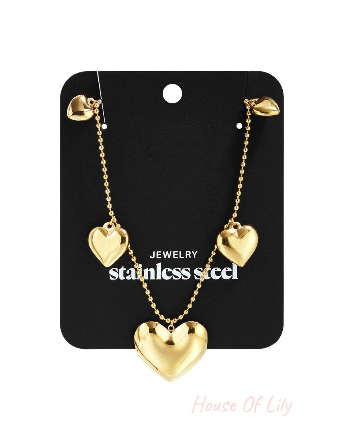 Gold-tone stainless steel chain necklace featuring three polished heart charms on a black display card.