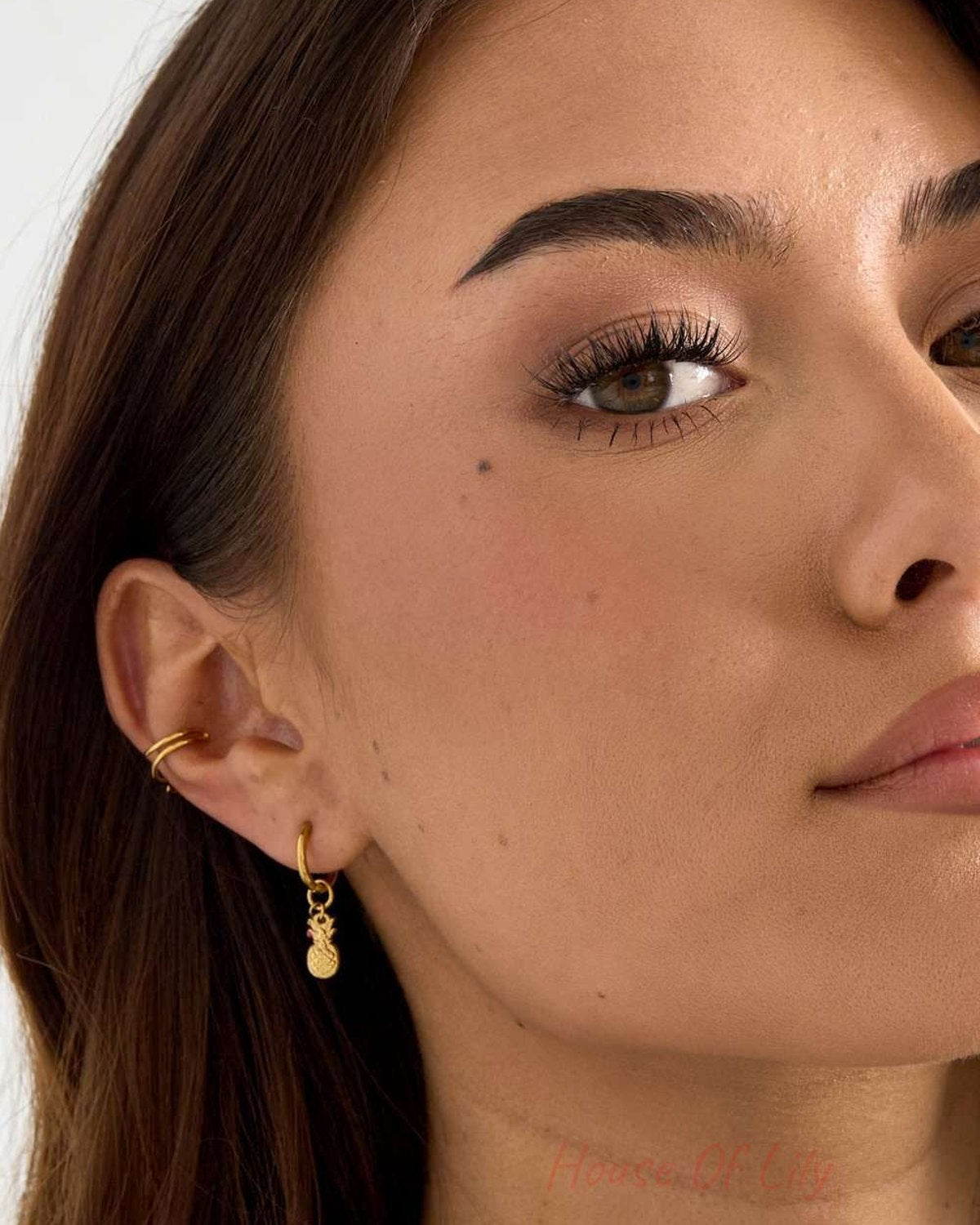 Model wearing Pineapple Aura Drops: a small gold hoop earring with a dangling textured pineapple charm.