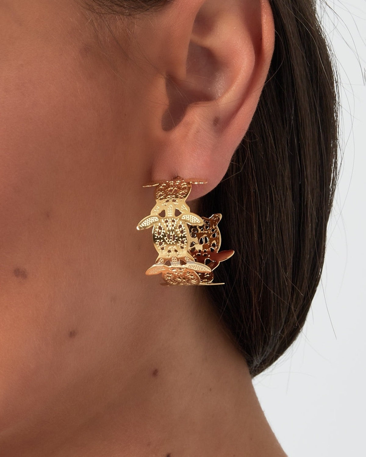 Close-up view of a woman wearing gold-plated turtle motif hoop earring on her ear