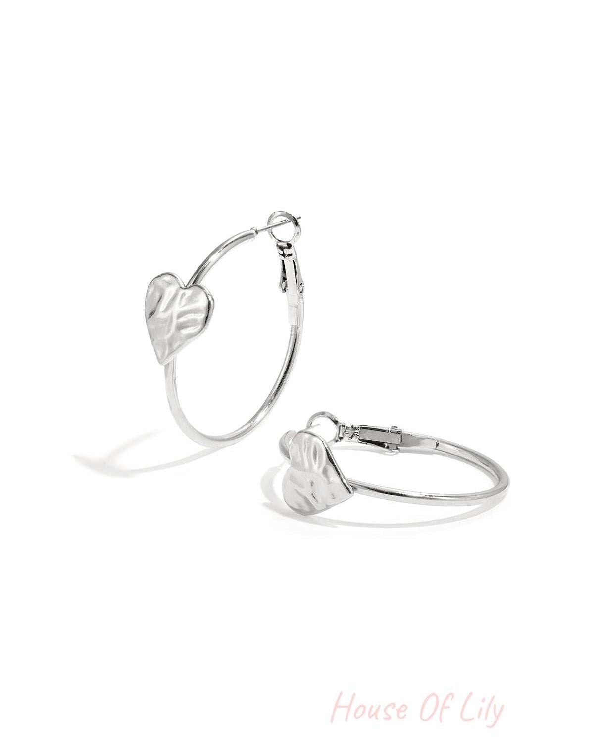 Silver hoop earrings with textured heart detail on white background