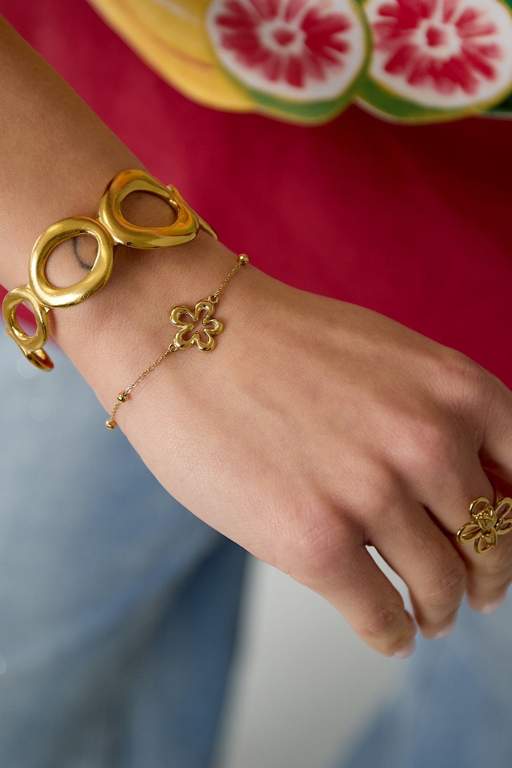 Gold-toned Elegant Floral Charm Bangle worn with a matching delicate flower chain bracelet and a floral ring.
