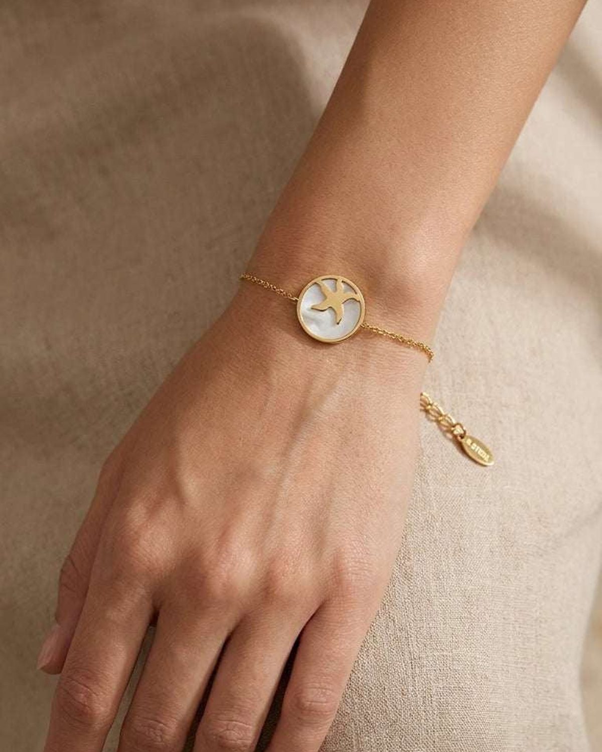 Gold chain bracelet featuring a round pendant with a white mother-of-pearl inlay and a gold starfish silhouette.