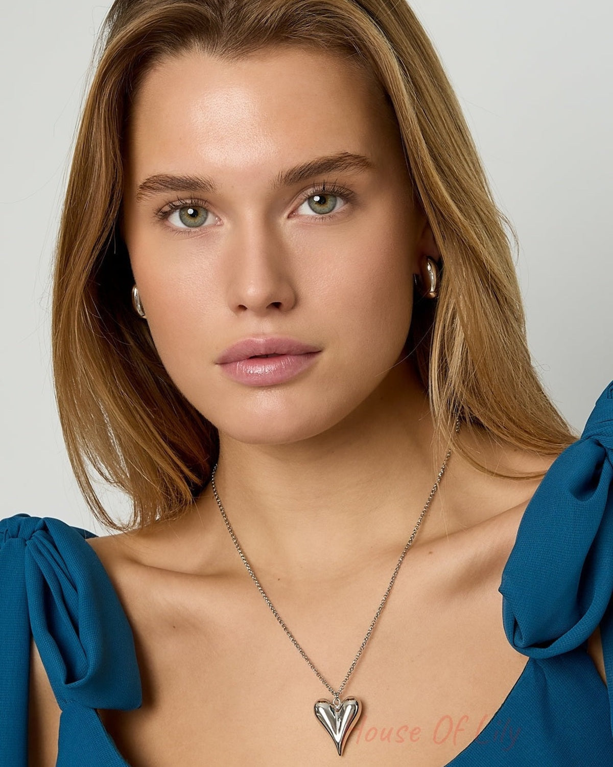 Close-up portrait of a woman wearing a silver-tone puffy heart pendant necklace with a blue off-shoulder top