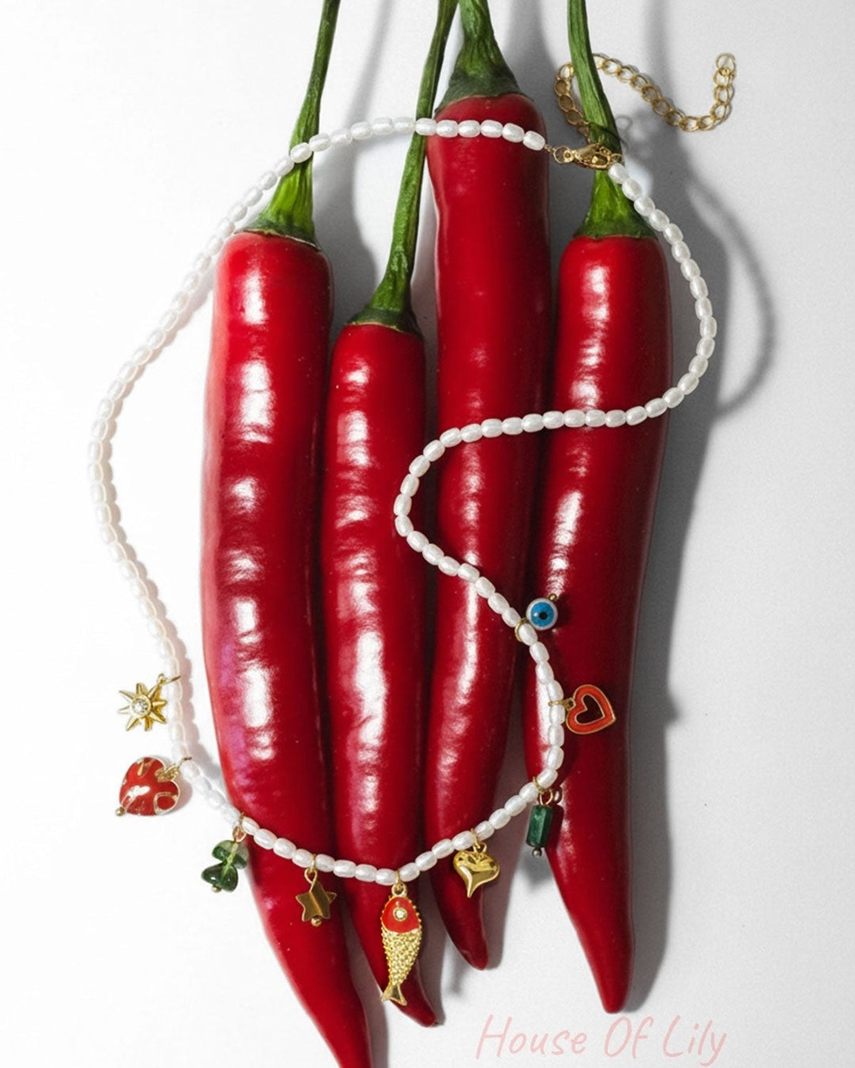 The beaded charm necklace creatively draped over bright red chili peppers showing playful design