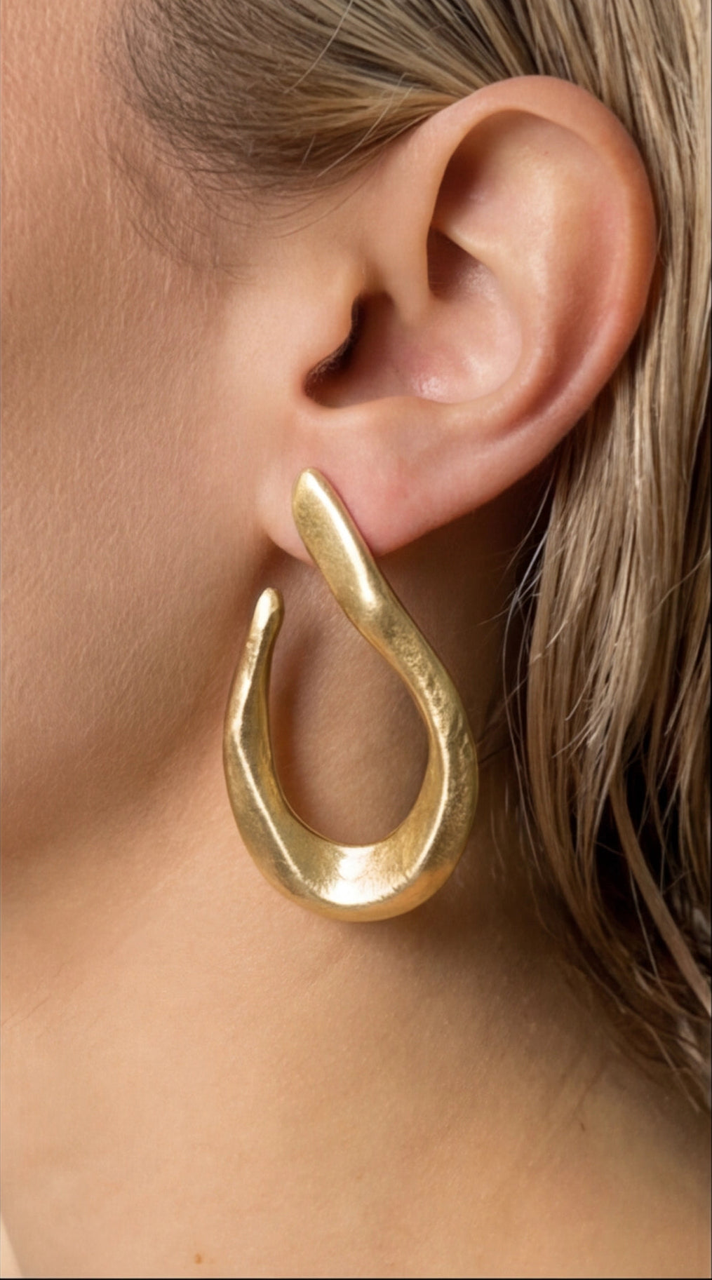 Gold hoop earring worn by a person with blonde hair.