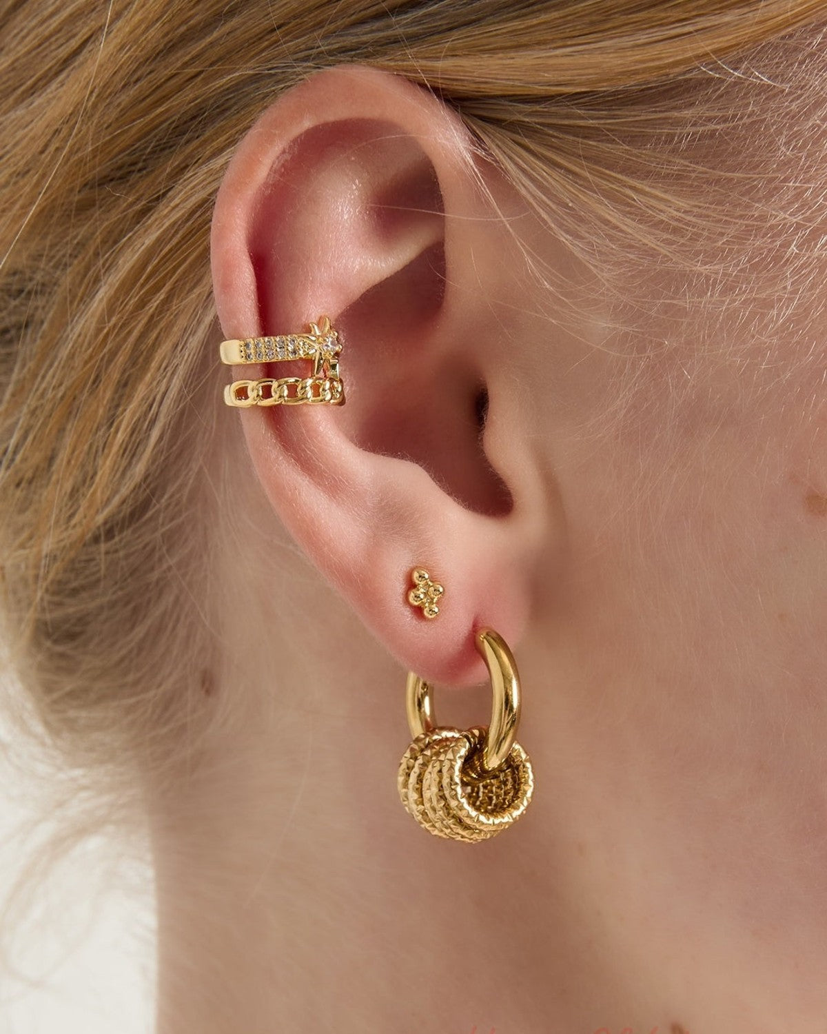 Close-up of a woman wearing gold textured hoop drop earrings with additional gold ear cuffs