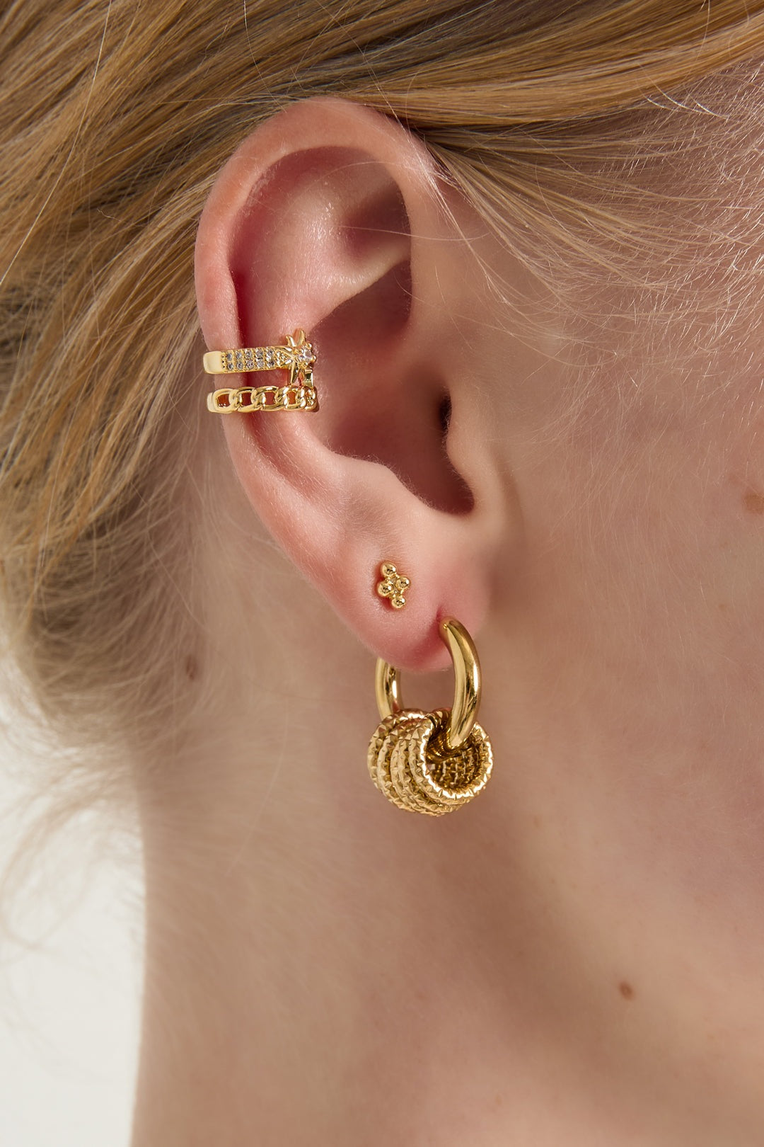 Close-up of a woman wearing gold textured hoop drop earrings with additional gold ear cuffs