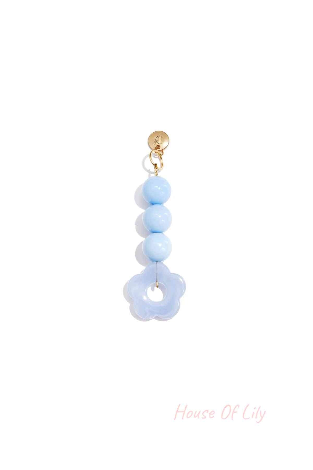 Light blue acrylic flower bag charm with three round light blue beads hanging from a gold clasp on white background