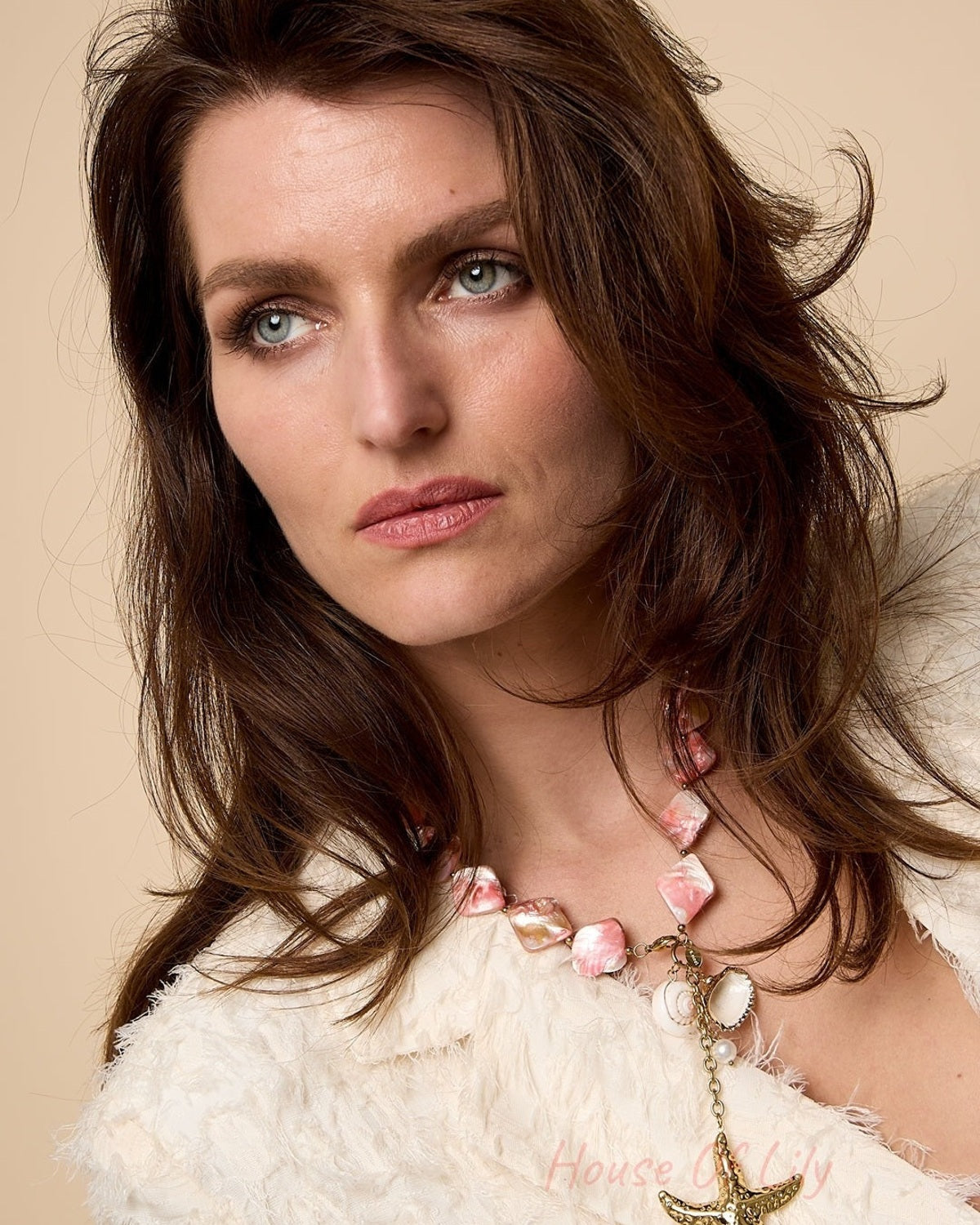 Close-up portrait of woman wearing pink and cream shell bead necklace with starfish charm against beige background