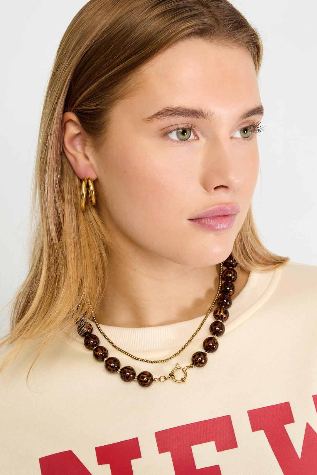Model wearing the leopard print acrylic beaded necklace paired with gold hoop earrings and a cream-colored top with red lettering