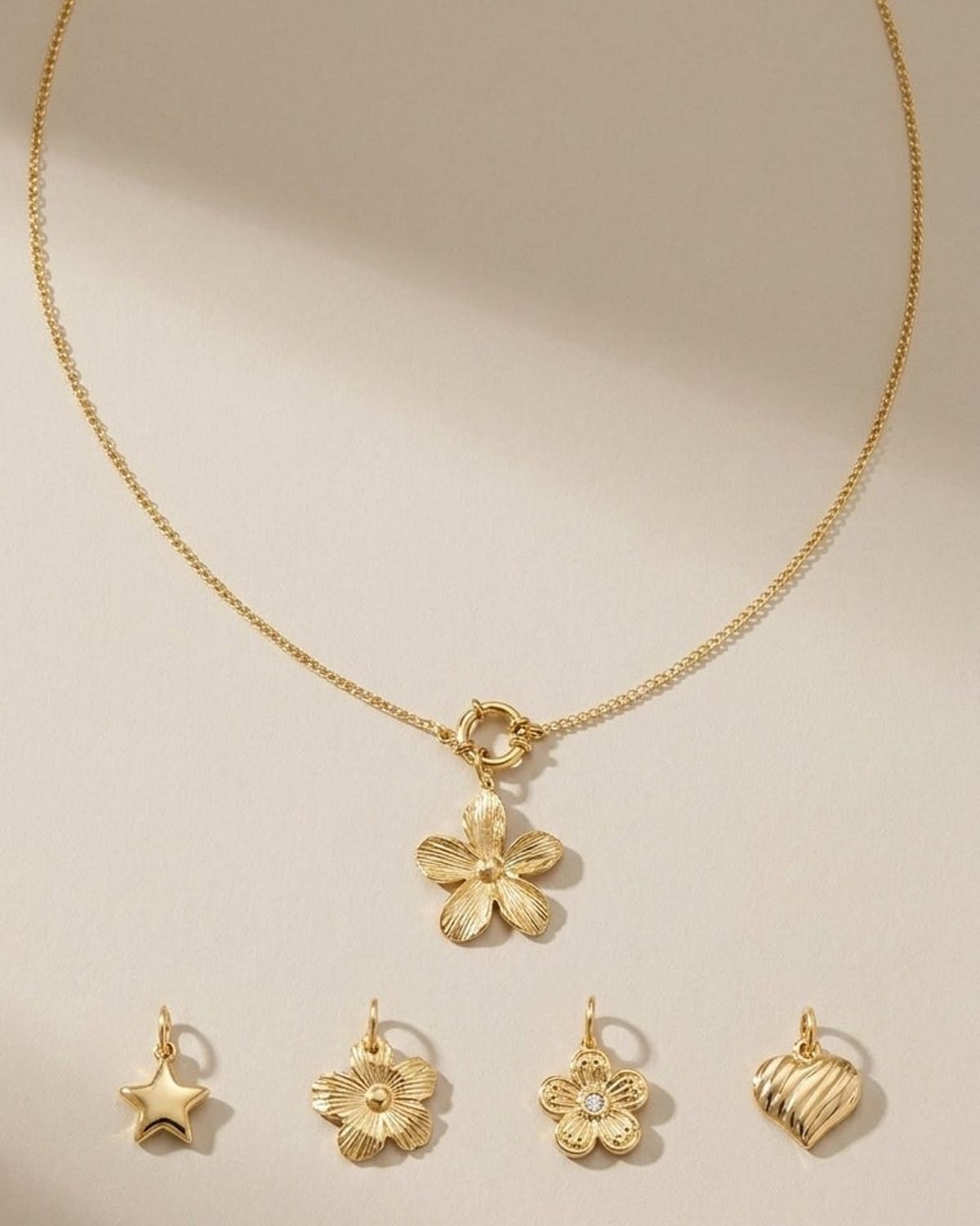 Gold chain necklace with flower pendant and four additional charms: star, textured flower, jeweled flower, and heart.