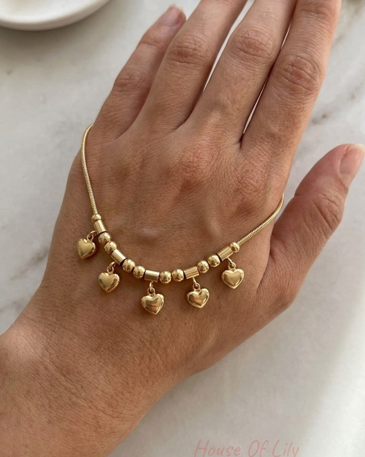 Gold chain bracelet on a hand featuring beads and dangling heart charms.