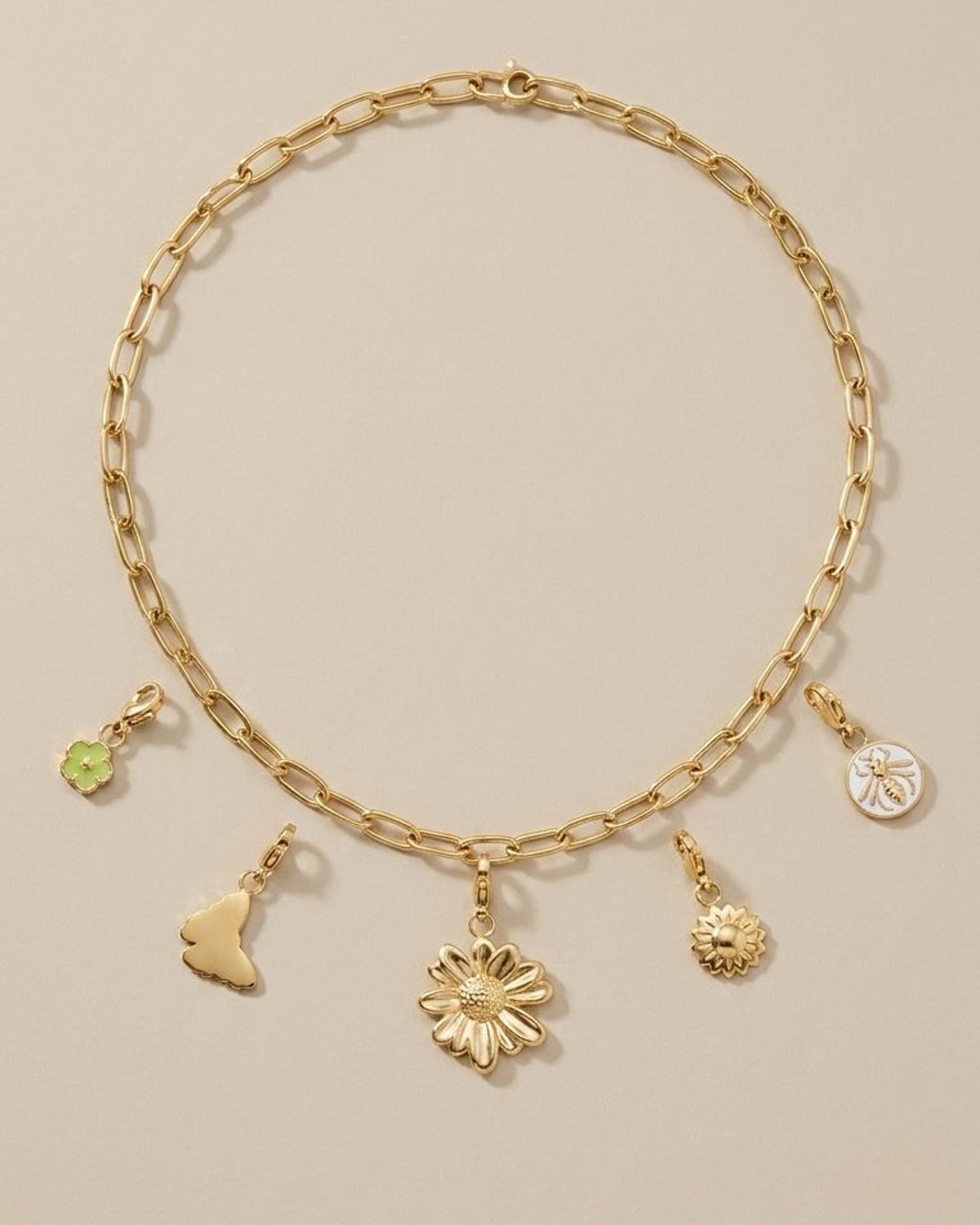 Gold chain necklace with five charms: a green flower, butterfly, large flower, small sun, and a bee on white enamel.