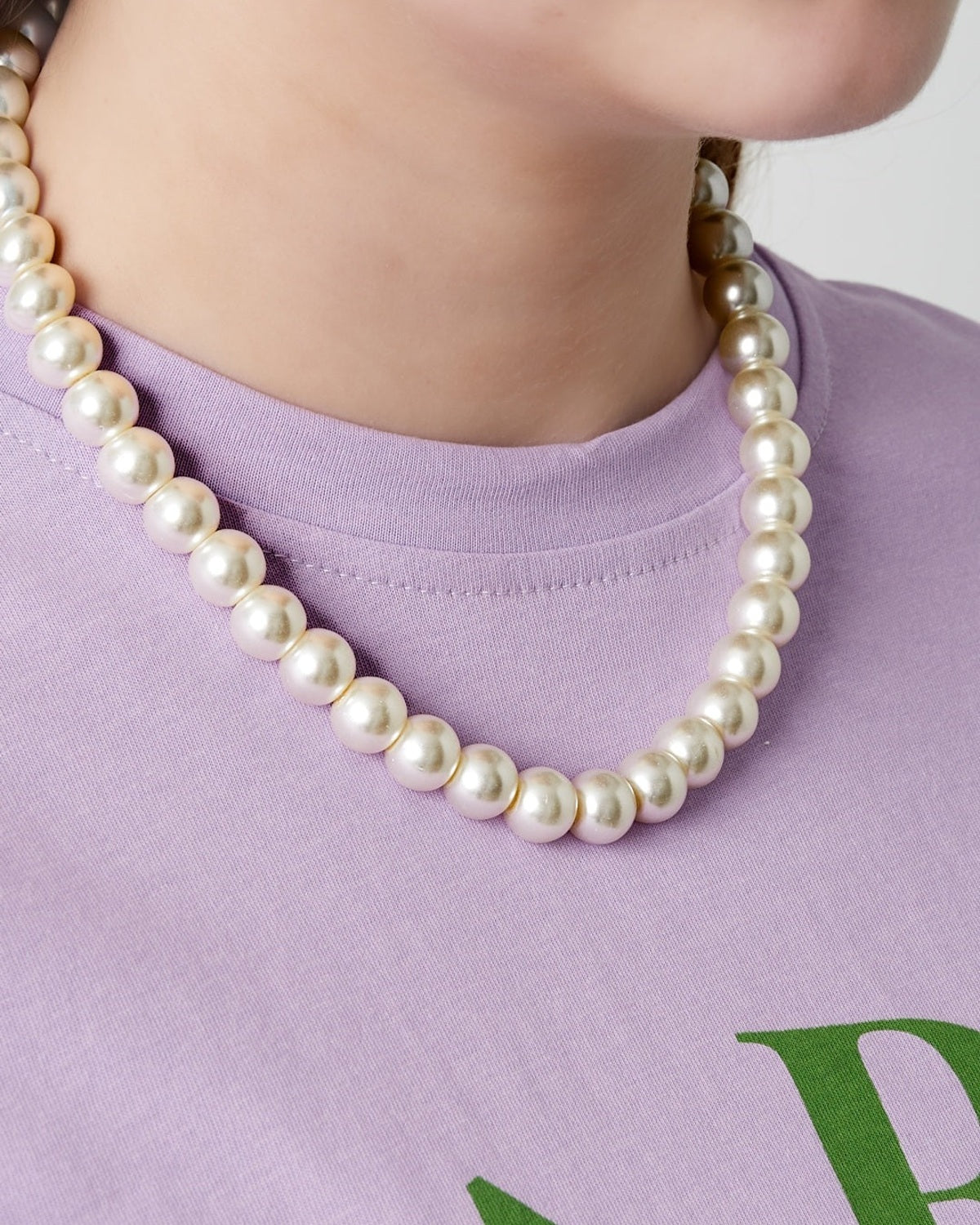Model wearing a short pearl beaded necklace paired with a light purple shirt featuring green letters
