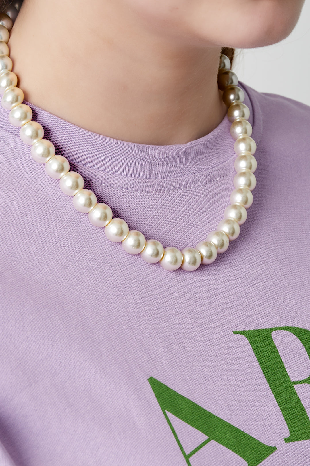 Model wearing a short pearl beaded necklace paired with a light purple shirt featuring green letters