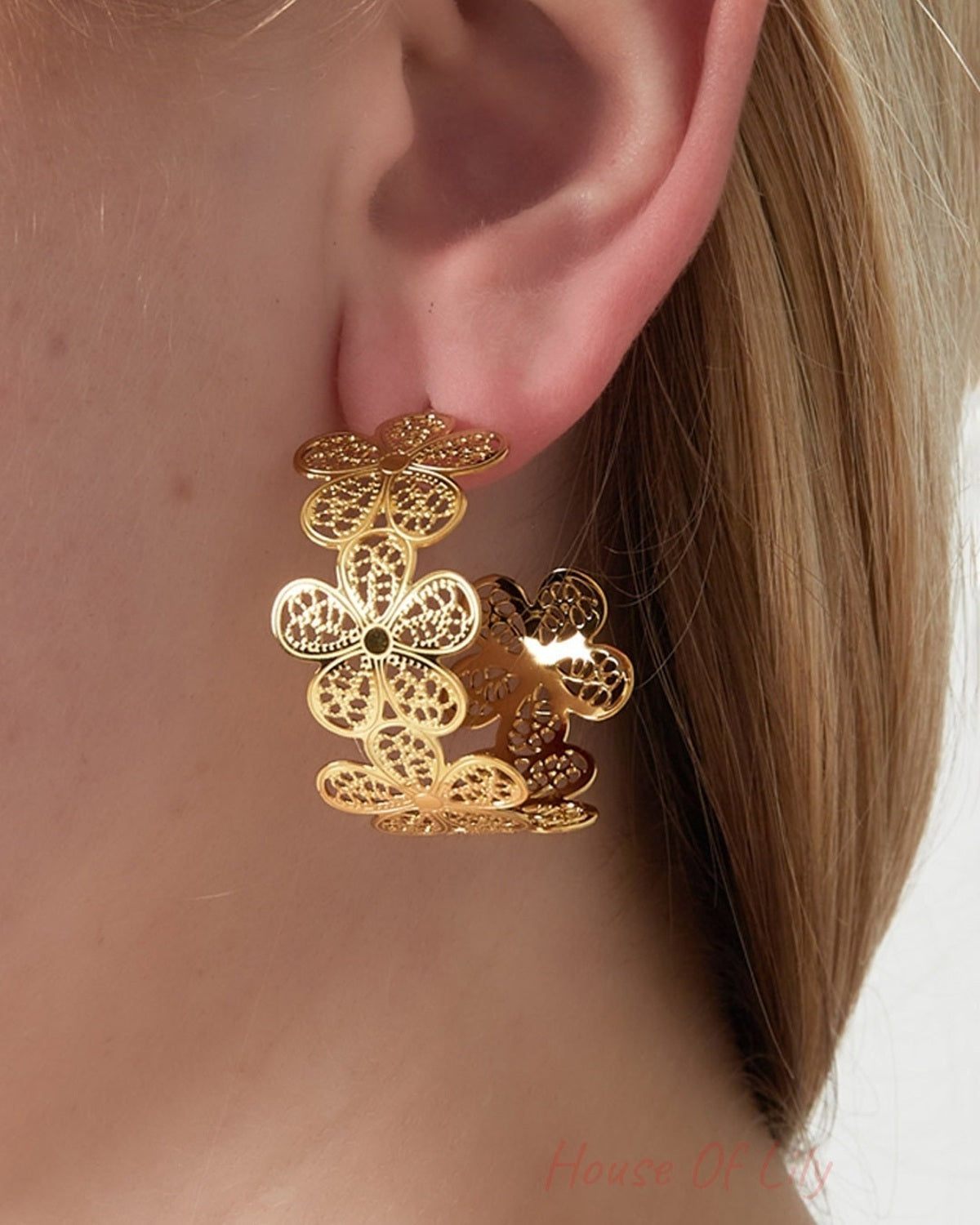 Close-up of a woman wearing gold floral hoop earrings with intricate flower cut-outs