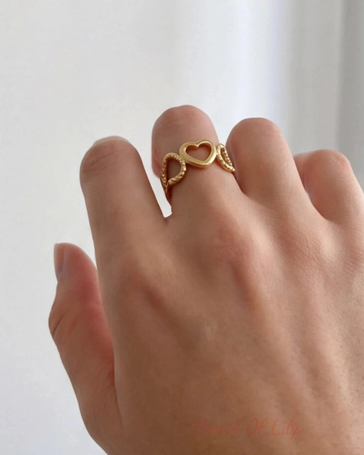 Gold heart-shaped ring on a person's finger against a white background