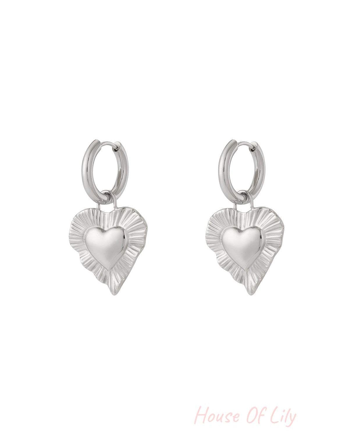 Pair of silver drop earrings with radiant heart-shaped charms featuring a textured fluted border on white background.