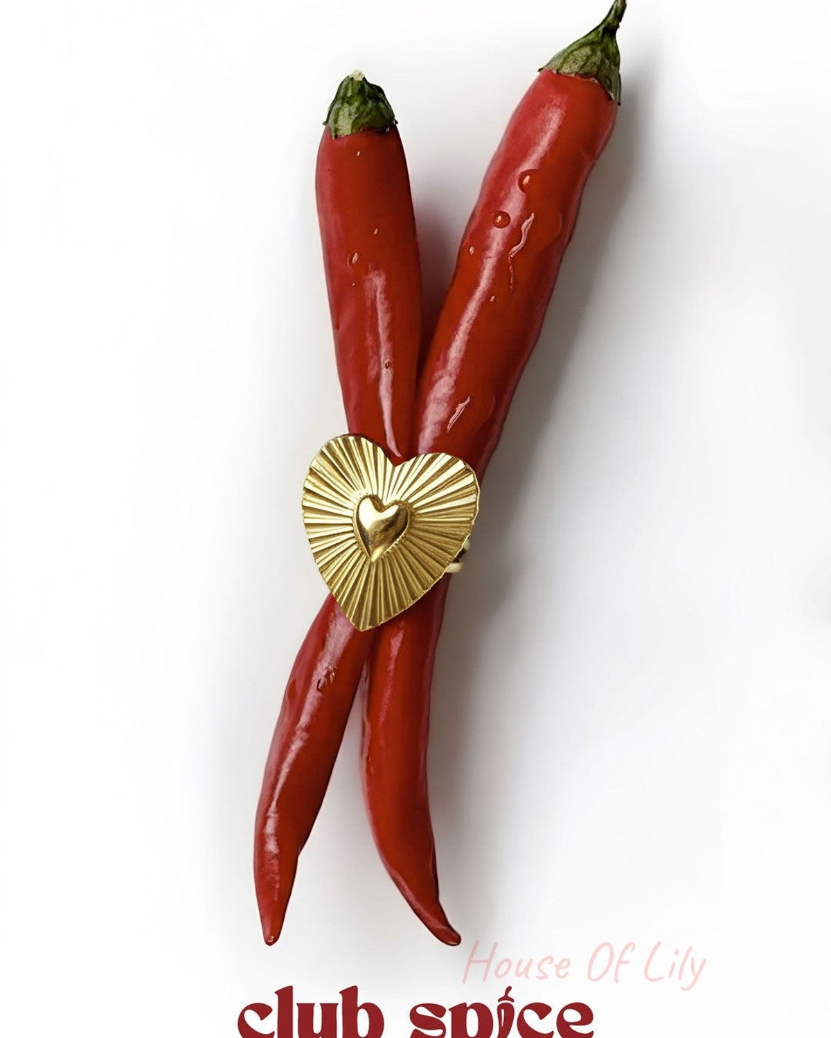 Gold heart-shaped statement ring styled creatively across two red chili peppers with 'club spice' text below
