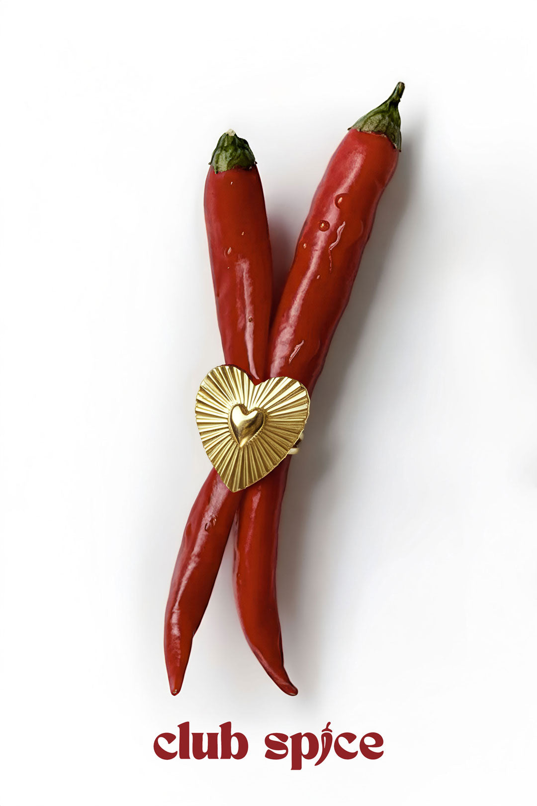 Gold heart-shaped statement ring styled creatively across two red chili peppers with 'club spice' text below