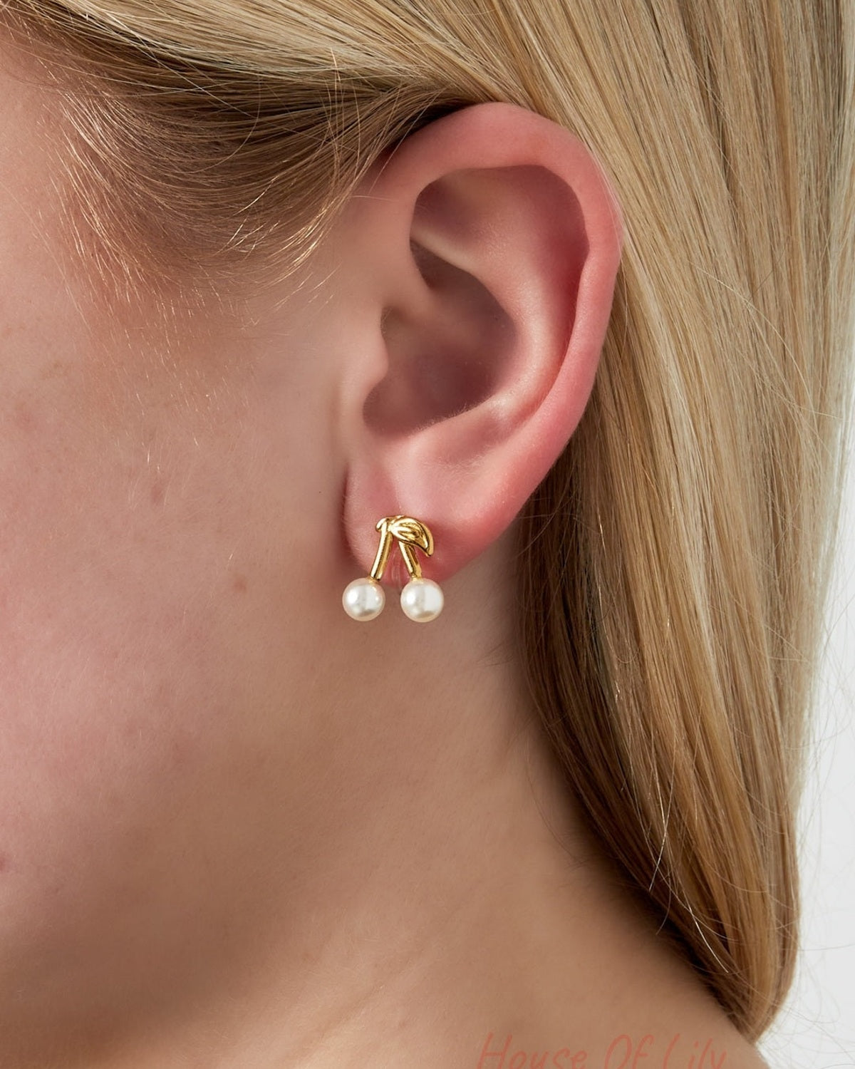Close-up of cherry clip earrings worn on ear, showing gold-tone stems and pearl details