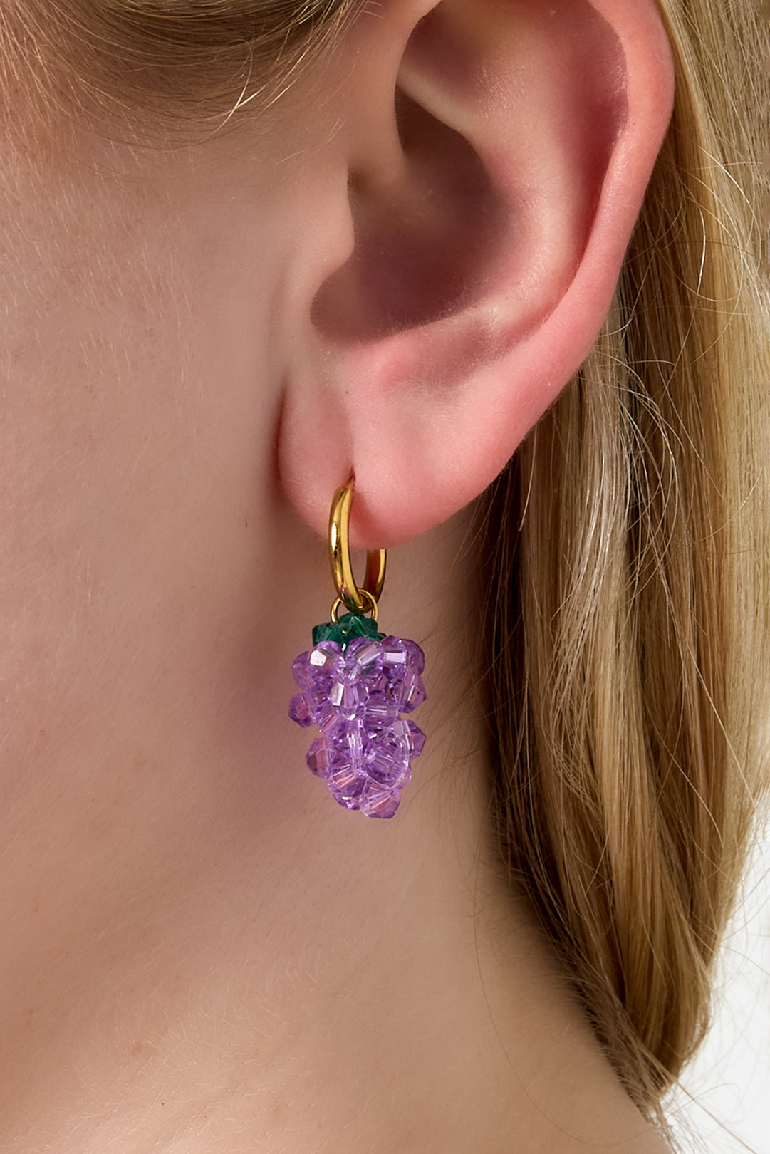 Model wearing gold hoop earrings featuring playful purple grape bead dangles.