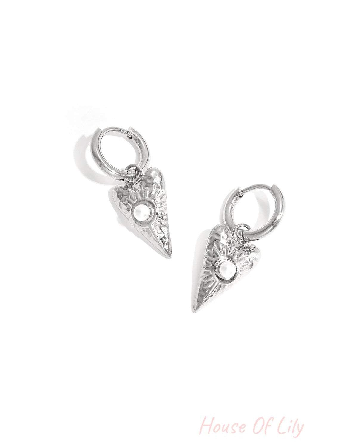 Close-up of silver heart-shaped drop earrings with pearl detail on white background