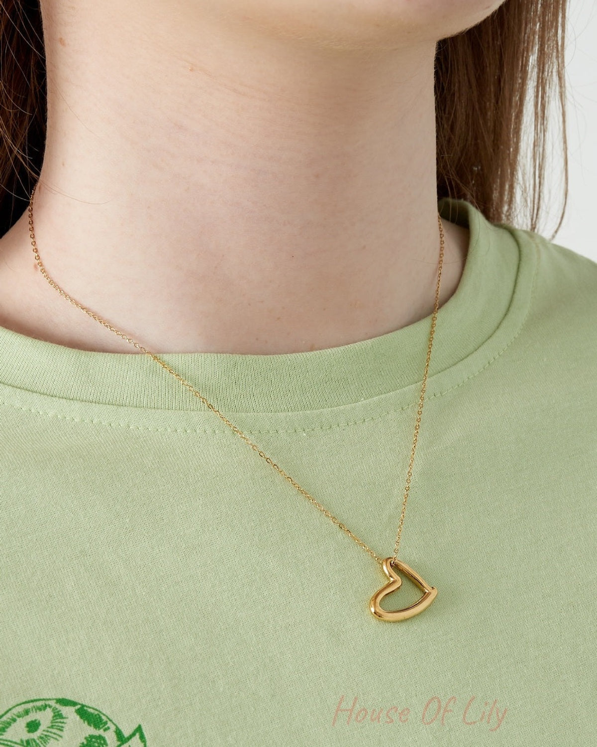 Close-up of woman wearing the gold heart pendant necklace with a light green top