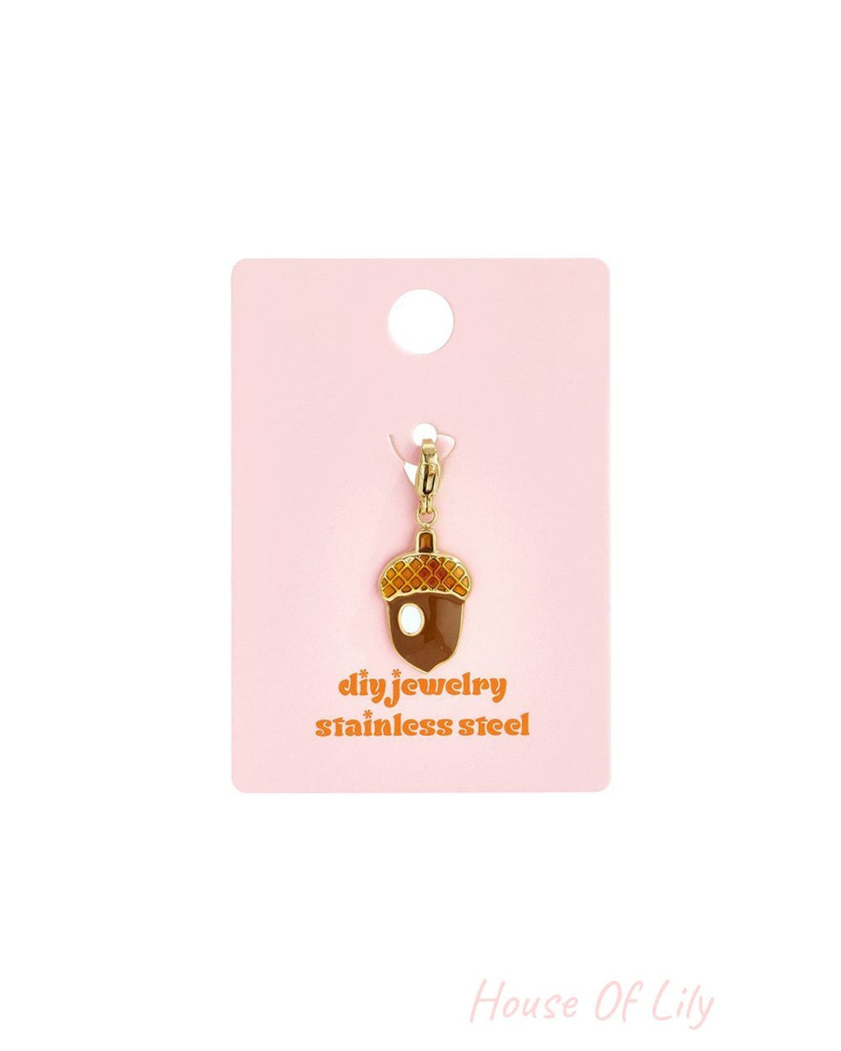 Cute Acorn Drop charm made of gold-tone stainless steel with brown and orange enamel details on a pink display card.