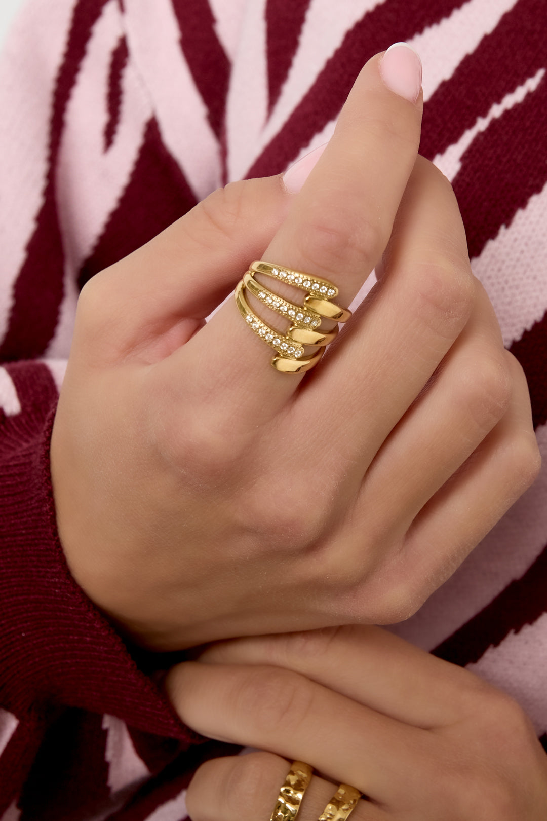 Close-up of a hand wearing the gold-tone multi-band statement ring paired with rings and burgundy patterned clothing