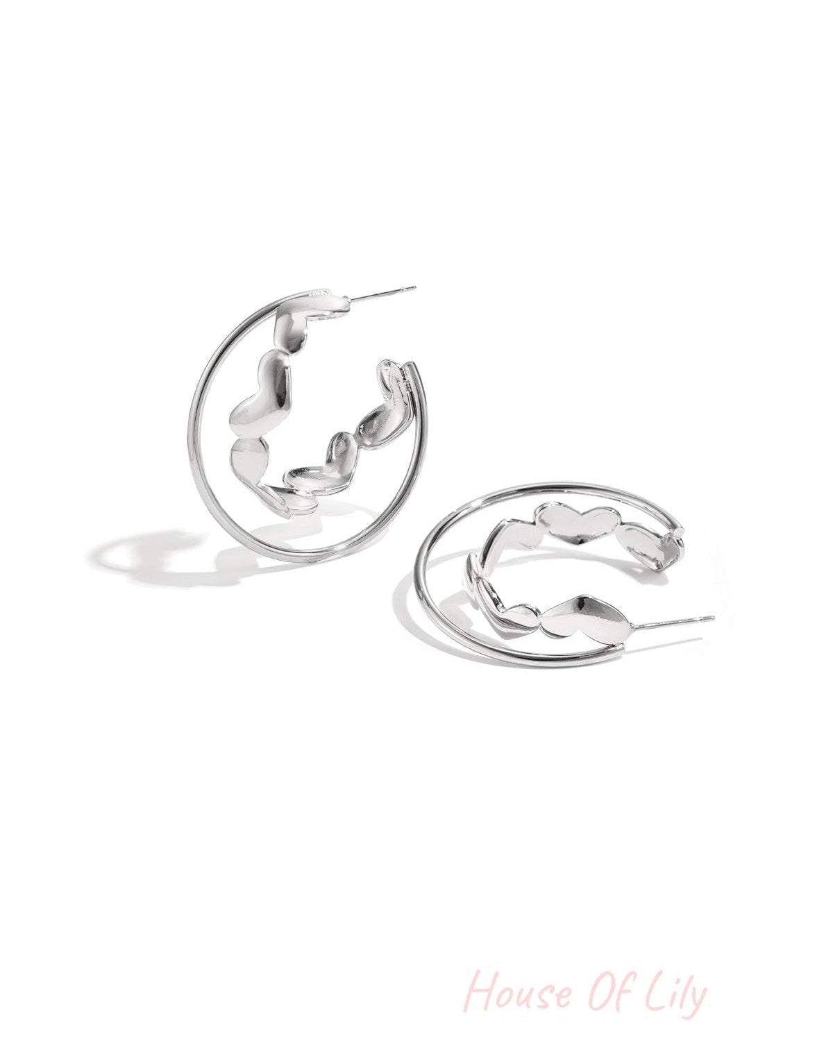 Silver hoop earrings with heart-shaped accents laid on white background