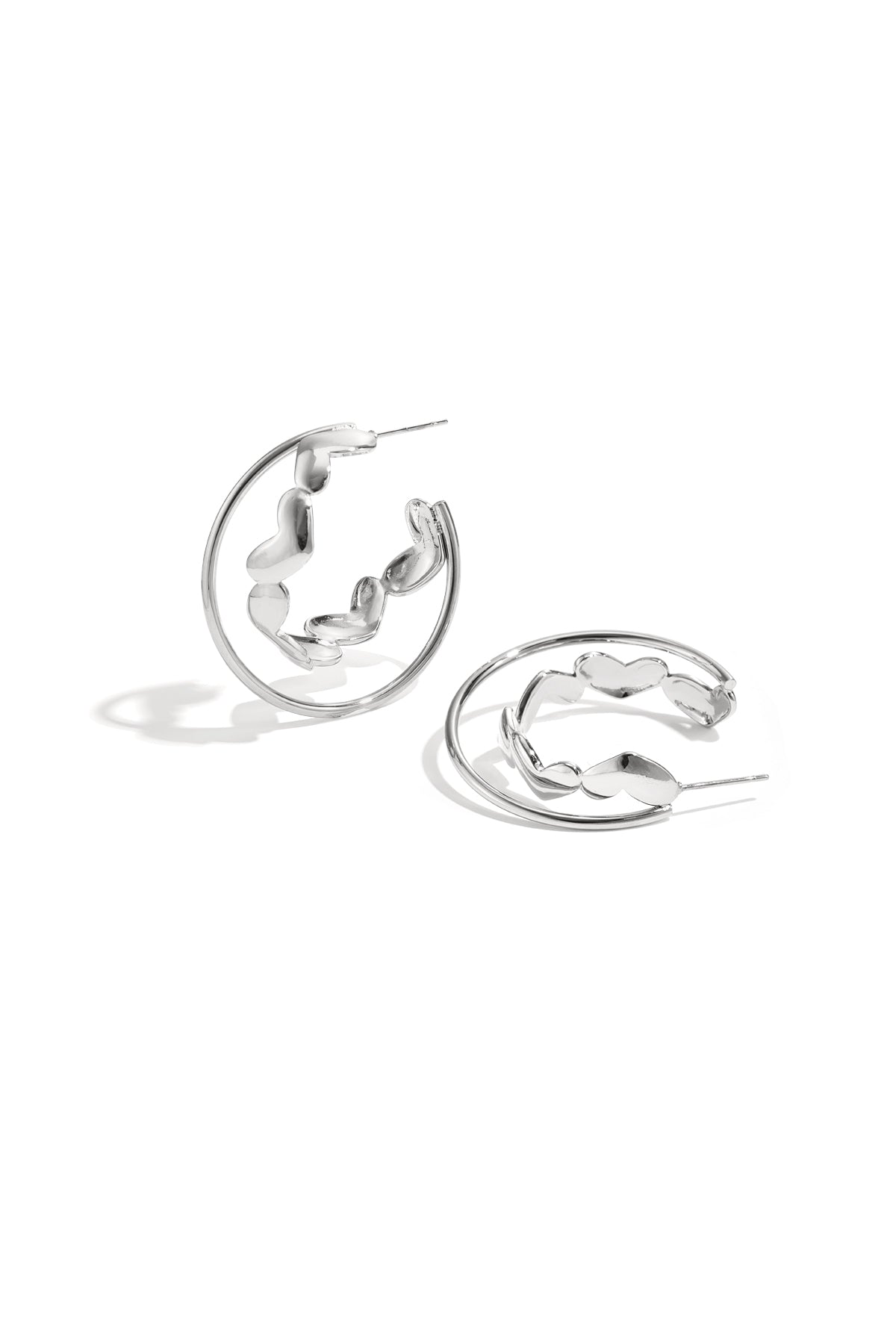 Silver hoop earrings with heart-shaped accents laid on white background