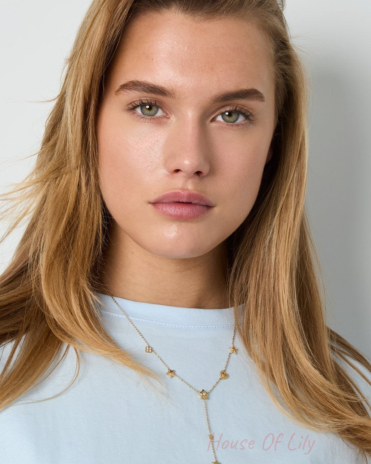 Model wearing a delicate gold lariat necklace featuring small star and heart charms with inset clear stones.