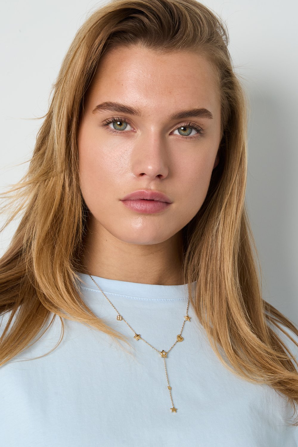 Model wearing a delicate gold lariat necklace featuring small star and heart charms with inset clear stones.