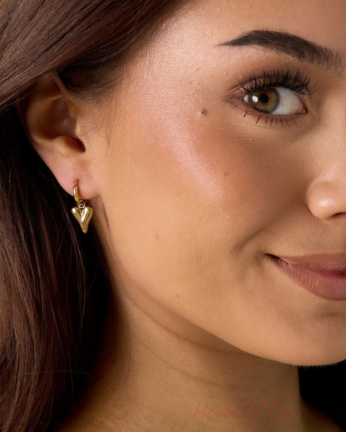Main Character Heart Drops: Small, polished gold hoop earrings featuring a dainty, puffed heart charm on a woman’s ear.