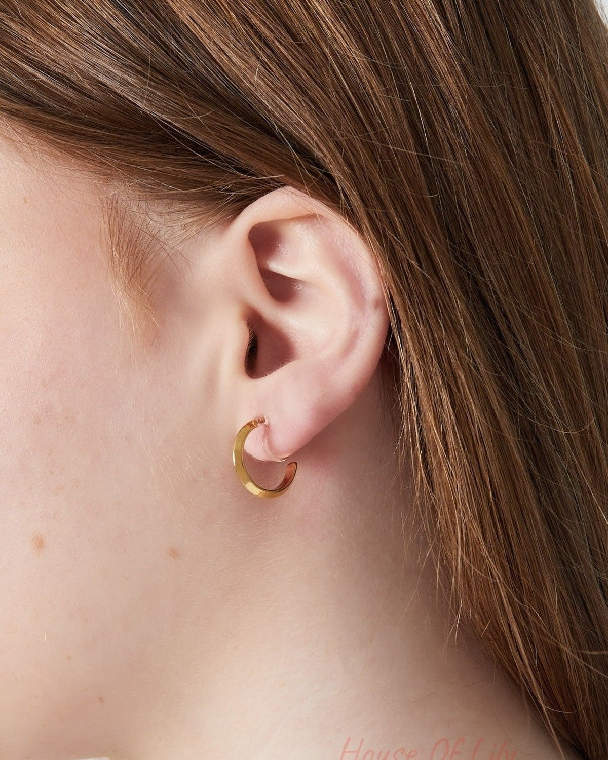 Close-up of a woman wearing a gold clip-on hoop earring featuring a sleek and simple design