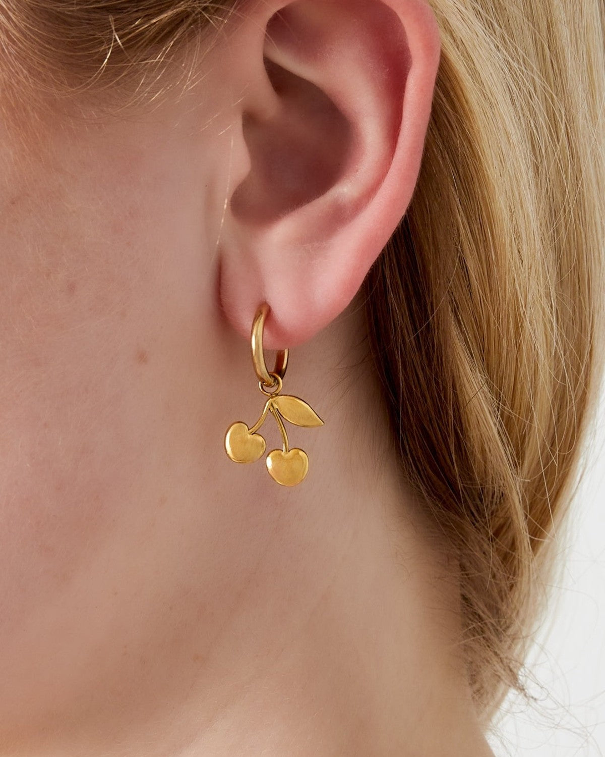 Close-up of a woman's ear wearing a gold-tone cherry charm drop earring showcasing its delicate design