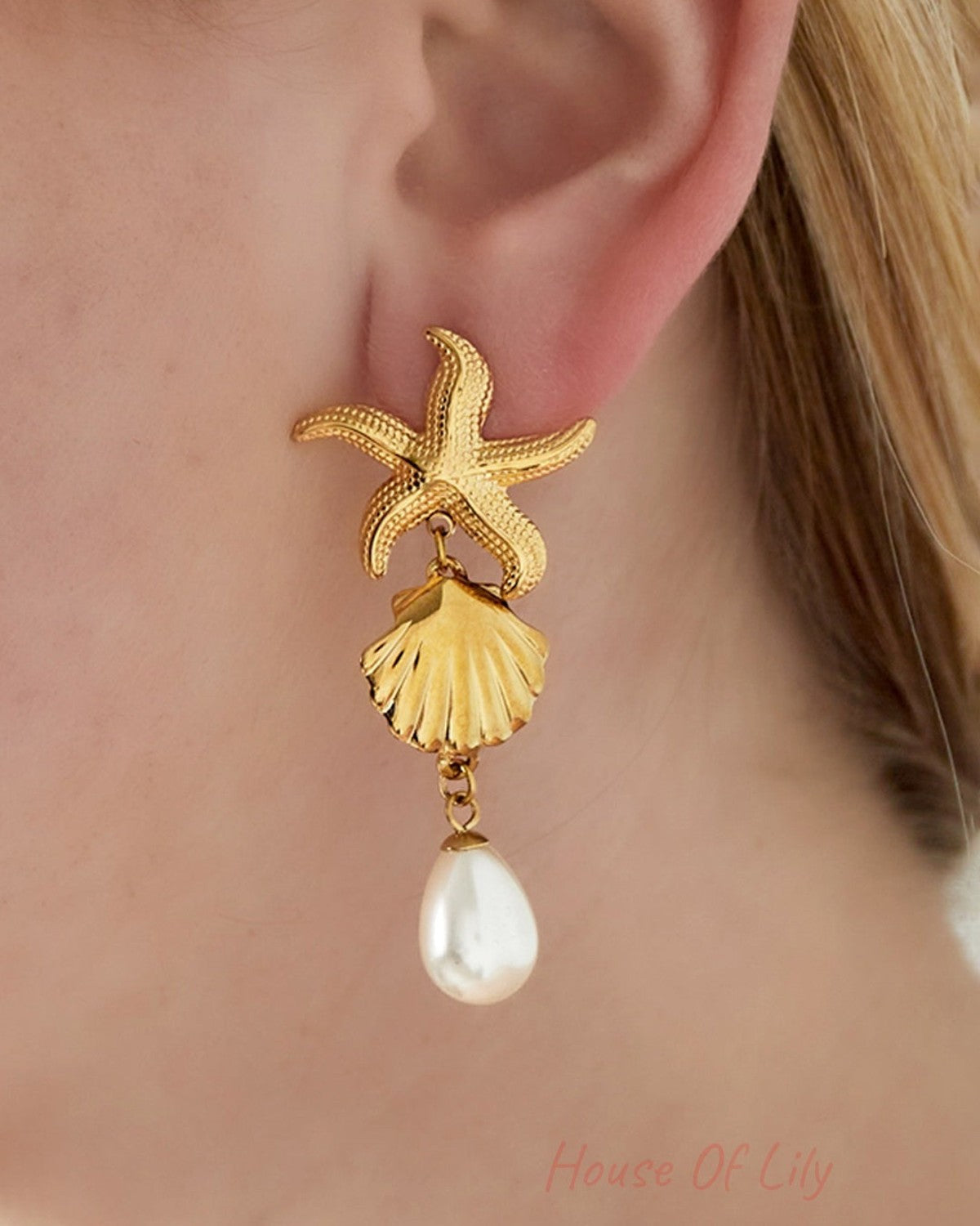 Close-up of gold starfish seashell earrings worn on ear with pearl drop