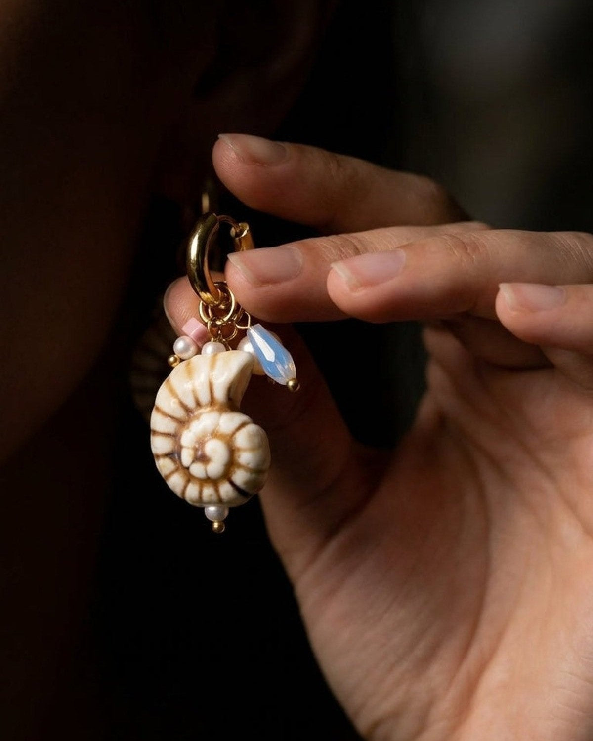 Shell Hoop Drop Era earring features a spiral shell charm, opal-like teardrop, and pearl accents on a gold hoop.