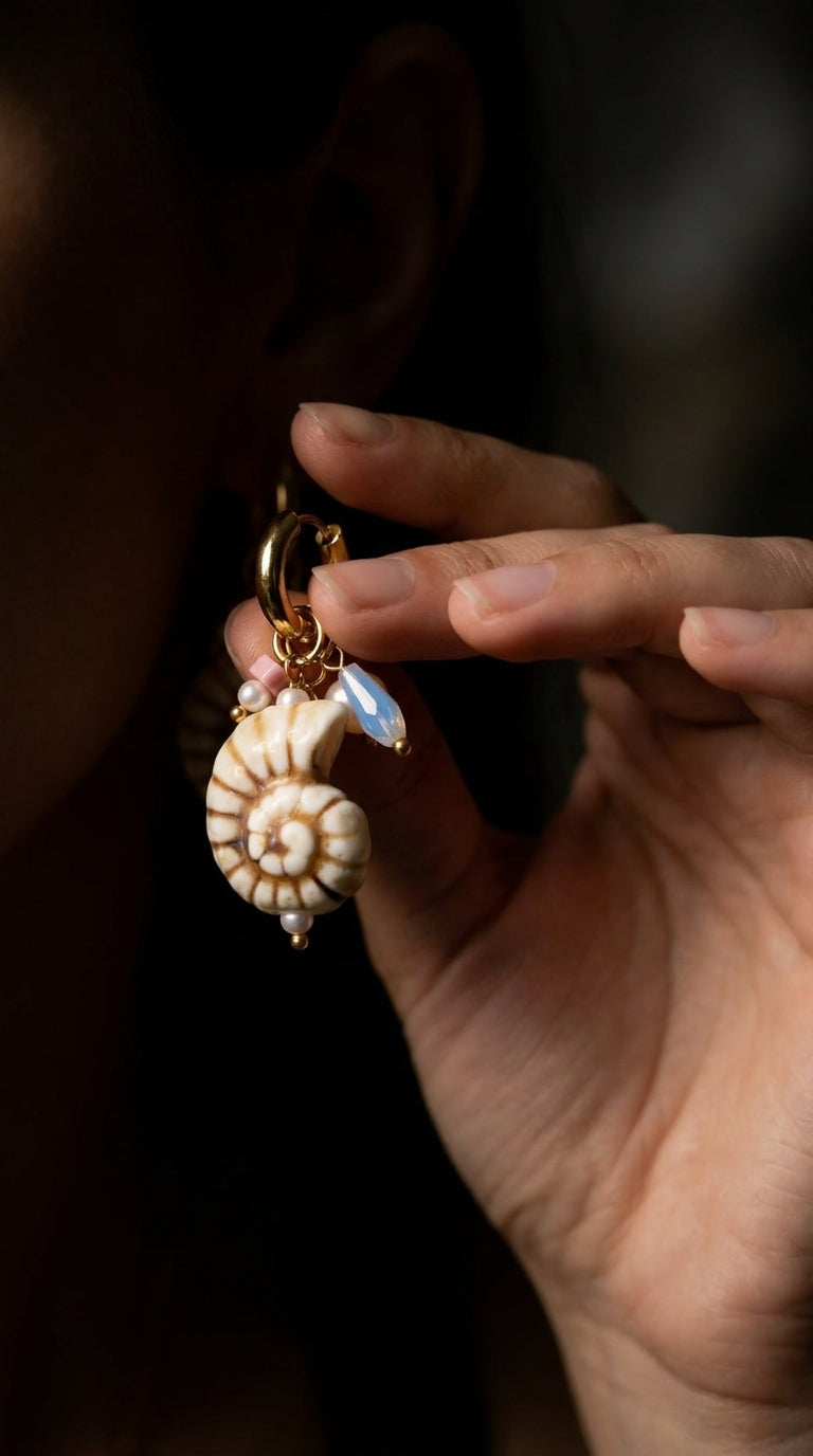 Shell Hoop Drop Era earring features a spiral shell charm, opal-like teardrop, and pearl accents on a gold hoop.