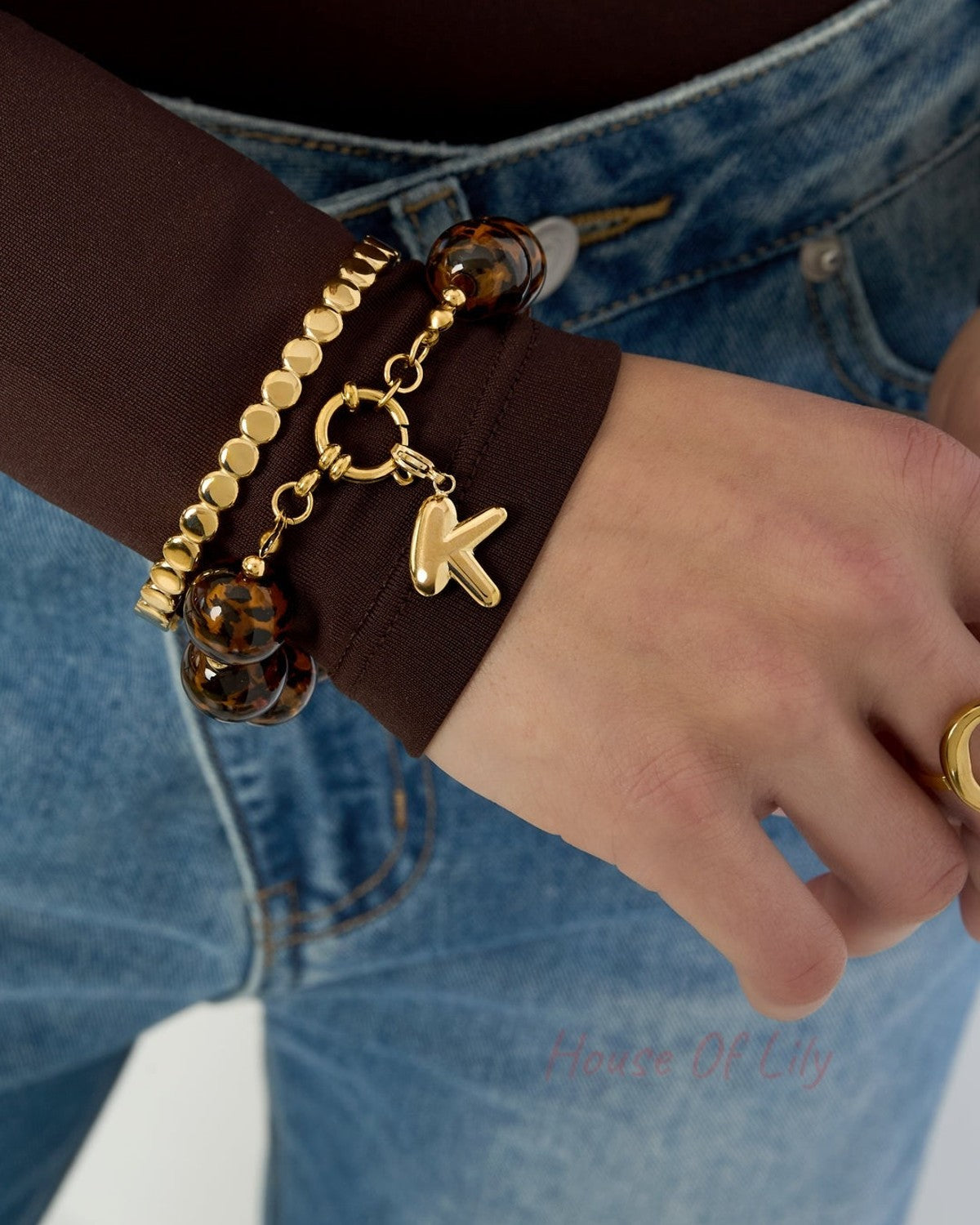 Bracelet worn on wrist paired with gold beads bracelet and gold ring, styled with brown top and denim jeans