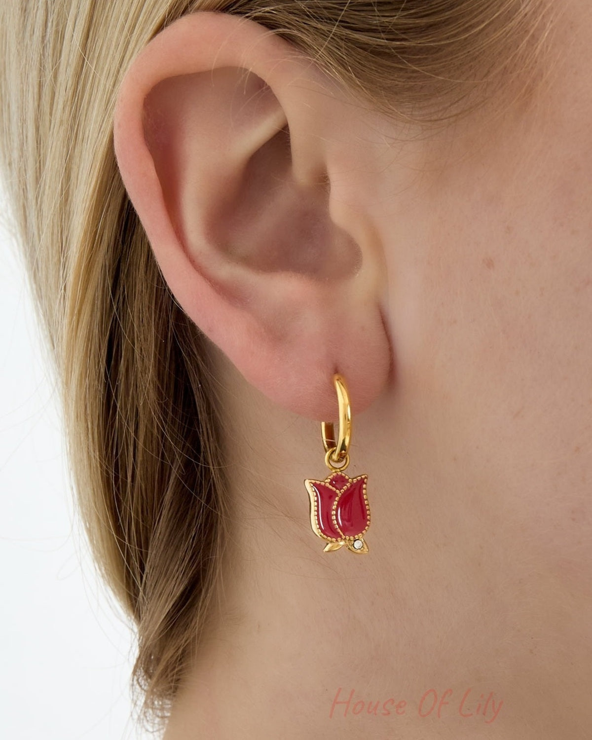 Close-up of woman wearing gold hoop earrings with red enamel tulip flower charms