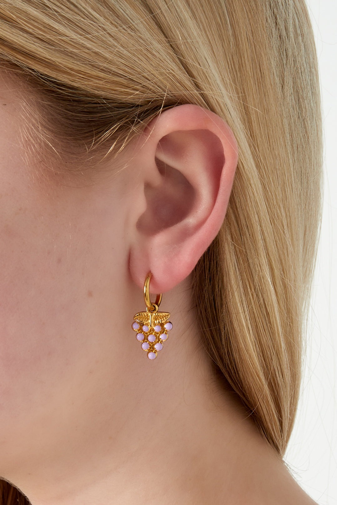Close-up of gold grape drop earring with pastel pink enamel worn on a woman's ear