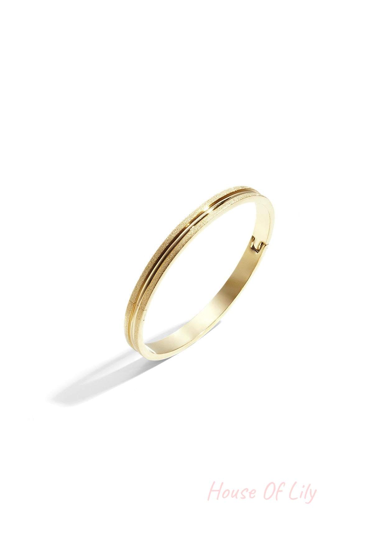 Gold-tone textured bangle bracelet with dual surface finish isolated on white background