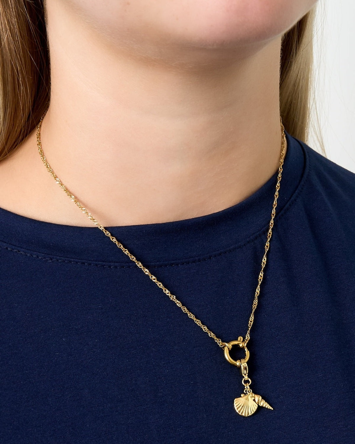 Model wearing gold chain necklace with seashell and spiral shell charms over navy top