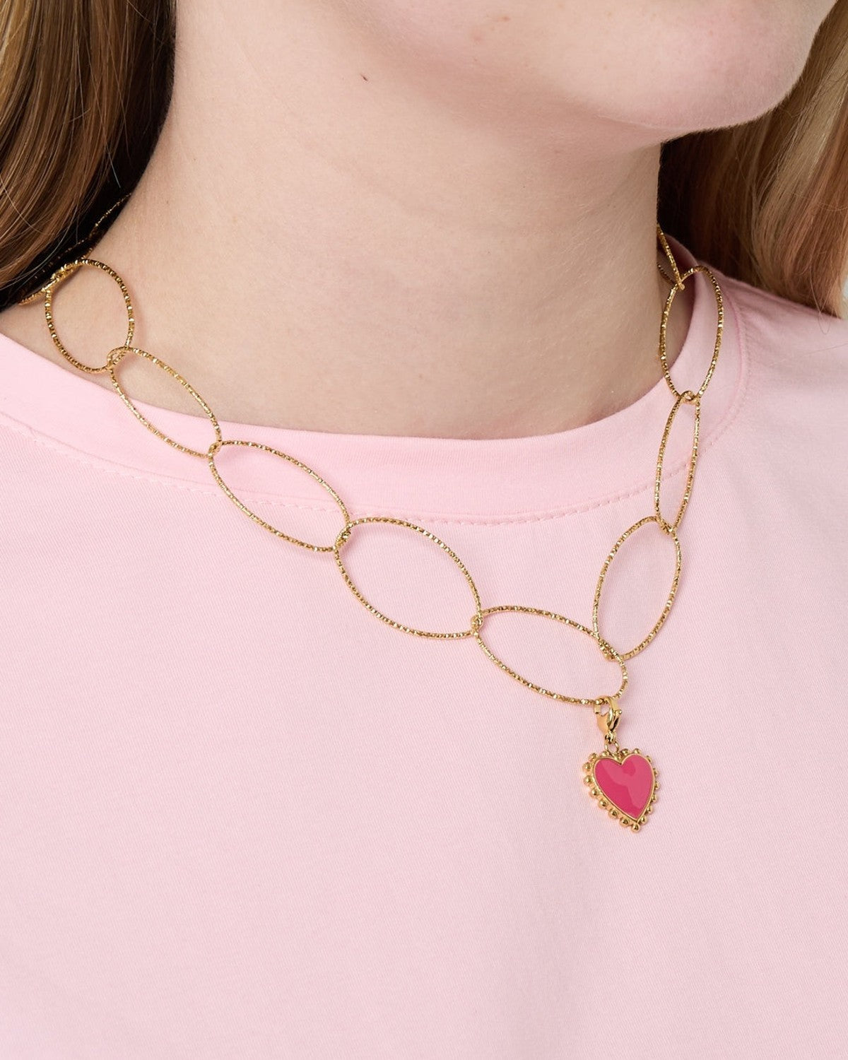 Woman wearing gold chunky oval link necklace with pink heart pendant over light pink shirt