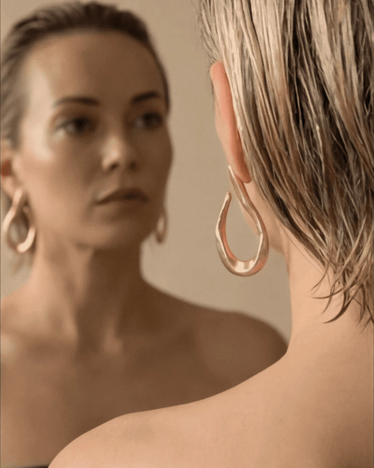 Woman wearing gold hoop earrings looking at herself in a mirror.