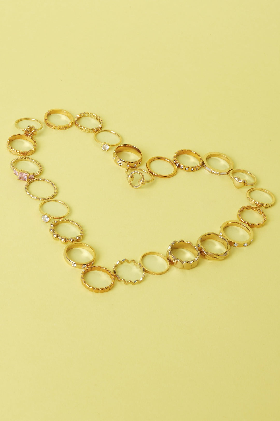Collection of various gold rings with different designs and textures arranged on yellow background